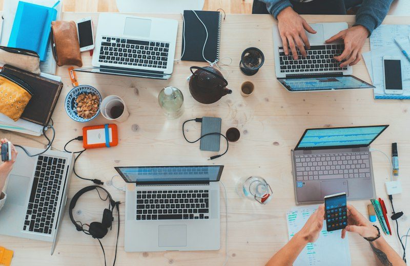 Arbeitstisch von oben mit Laptops und Notizen mehrerer Personen
